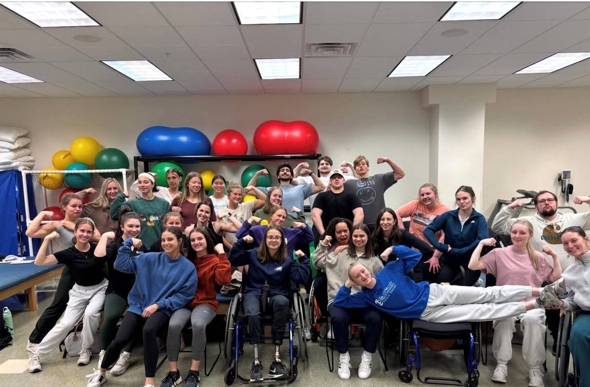 Group of young adults smiling at the camera, some of which are flexing their arm muscles.